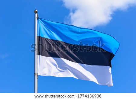 The flag of Estonia is a rectangular banner of three equal horizontal stripes of blue, black and white on a background of blue sky during the summer day.