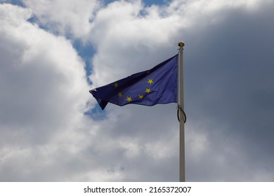 The flag of the European Union against the cloudy sky flutters with the wind.
