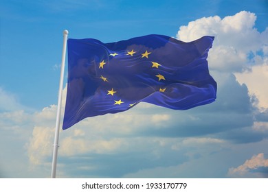 Flag of the European Union waving in the wind on flagpole against the sky with clouds on sunny day