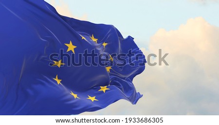 Flag of the European Union waving in the wind on flagpole against the sky with clouds on sunny day