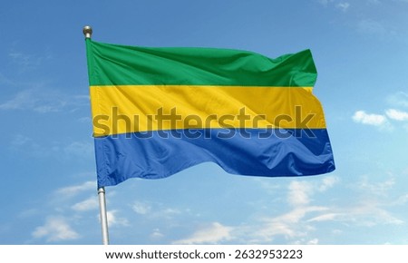 The flag of Gabon waves under a clear sky, featuring horizontal green, yellow, and blue stripes symbolizing nature, sunshine, and the sea.