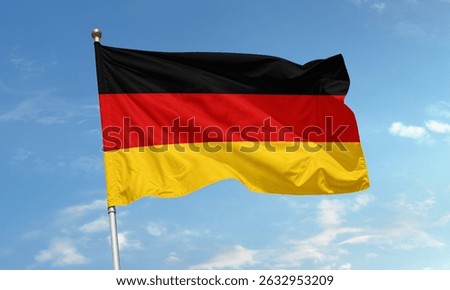 The flag of Germany waves in the wind under a clear sky, showing horizontal black, red, and gold stripes representing unity and freedom.