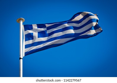Flag of Greece blowing in the wind on a pure sky blue background. National symbol showing white cross symbolising Eastern Orthodox Christianity. 