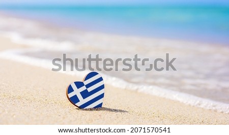 Flag of the Greece in the shape of a heart on a sandy beach. The concept of the best vacation in Greek resorts