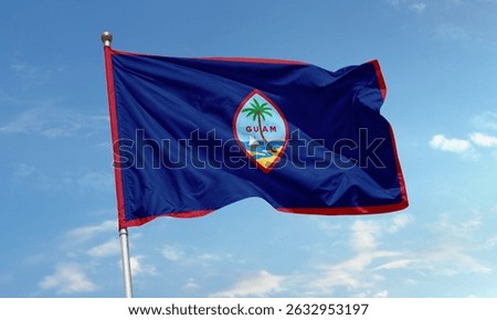 Flag of Guam featuring a blue background with a red border and island emblem, waving against a clear blue sky.