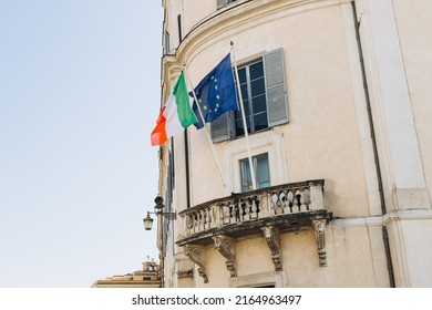 Flag Of Italy With EU Flag Hanging On The Balcony Of A House. Flags In The Facade Of Old Building