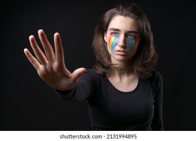 Flag LGBT Lizbian Woman With Rainbow Tears On Her Cheek Defends Herself With Her Hands In Front Of Her On A Black Background. The Girl Is Scared For Their Sexual Orientation. Discrimination Concept