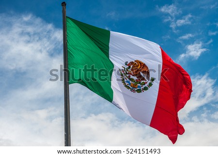 Flag of Mexico over blue cloudy sky