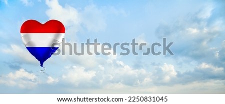 Flag of Netherlands on heart-shaped balloon against sky clouds background. Education, charity, emigration, travel and learning. Dutch language concept