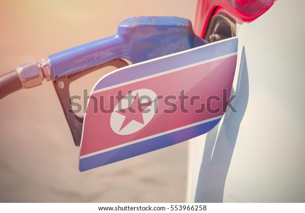 Flag of North Korea DPRK on the car\'s\
fuel filler flap with gas pump nozzle in the\
tank