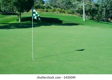 Flag on golf green with shadow, selective focus on the pin
