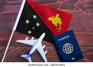 Flag of Papua New Guinea with passport and toy airplane on wooden background. Flight travel concept 
