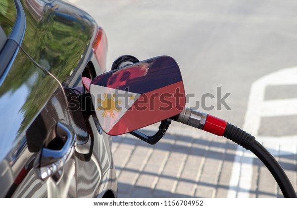 Flag of Philippines on the car\'s fuel\
tank filler flap. Fueling car with petrol pump at a gas station.\
Petrol station. Gasoline and oil products. Close\
up.