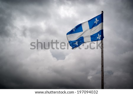 The flag of Quebec ( Fleurdelise ) waves in the wind in front of the tumultuous clouds of stormy skies.