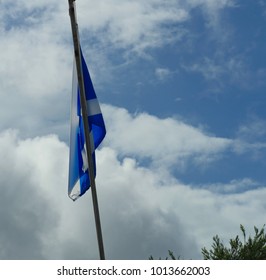 Flag of Scotland waving from a pole with blue and white clouds in the background