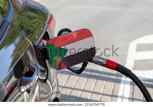 Flag of Sudan on the car\'s fuel tank\
filler flap. Fueling car with petrol pump at a gas station. Petrol\
station. Gasoline and oil products. Close\
up.