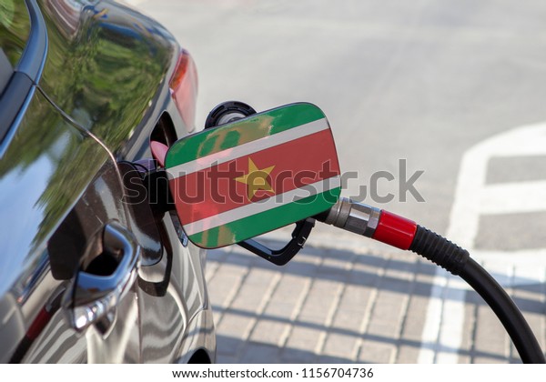 Flag of Suriname on the car\'s fuel\
tank filler flap. Fueling car with petrol pump at a gas station.\
Petrol station. Gasoline and oil products. Close\
up.