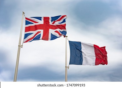 Flag of the United Kingdom and the flag of the Republic of France fluttering in the wind against a blue sky. The concept of friendship or cooperation of Great Britain and France.