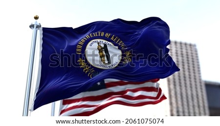 the flag of the US state of Kentucky waving in the wind with the American stars and stripes flag blurred in the background. Kentucky was admitted into the Union as the 15th state on June 1, 1792