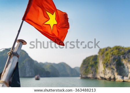 The flag of Vietnam (red flag with a gold star) fluttering on ship in the Halong Bay at the Gulf of Tonkin of the South China Sea, Vietnam. Karst towers-isles and blue sky are visible in background.