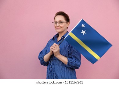 Curaçao Flag. Woman Holding Curacao Flag. Nice Portrait Of Middle Aged Lady 40 50 Years Old Holding A Large Flag Over Pink Wall Background On The Street Outdoors.