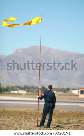 A flagman checks the wind direction so aid the landing of an airplane along an airstrip
