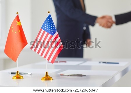 Flags of China and America against background of handshakes of political representatives of these countries. Concept of bilateral political relations and cooperation between United States and China