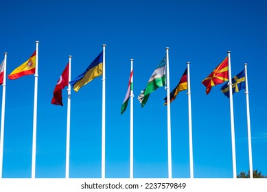 Flags of Different Countries Hang On Flagpoles Against Blue Sky. Flag of Spain, Ukraine, Germany, Sweden, Turkey, Uzbekistan and Macedonia. The concept of support and unity of countries. High quality