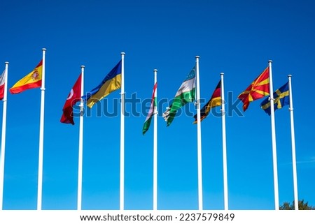 Flags of Different Countries Hang On Flagpoles Against Blue Sky. Flag of Spain, Ukraine, Germany, Sweden, Turkey, Uzbekistan and Macedonia. The concept of support and unity of countries. High quality