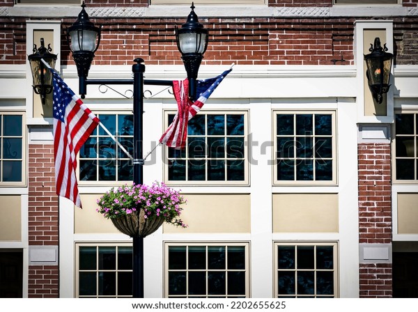 The flags and flowers on a light\
pole sitting on a city street in Manitowoc,\
Wisconsin.