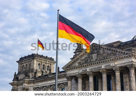 Flags of Germany are flying against the background of the sky and the Reichstag.