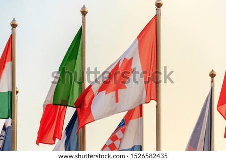 Flags hang on a flagpole. Background gray-blue sky. Canada, Italy.