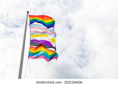 Flags for LBGTQi HBTQ rights. The Rainbow Pride Flag, The  Transgender Pride Flag, the Non-Binary Pride Flag in a row. On a flag pole waving in the wind, outdoors with clouds in the sky.