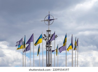 The Flags Of Ukraine And The European Union Are Fluttering In The Wind. Above Them, The NATO Symbol