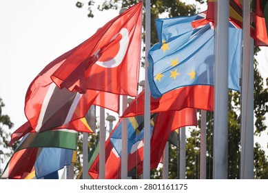 Flags of various countries are displayed on tall poles under sunshine. They are fluttering in the breeze, representing unity and diversity. This scene highlights international connections.