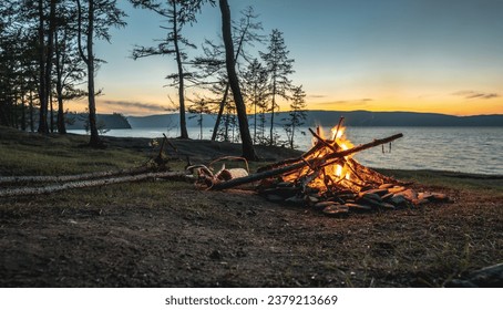 The flame of a bonfire on the background of the evening summer lake Baikal. Hiking trips to unique places of nature. - Powered by Shutterstock