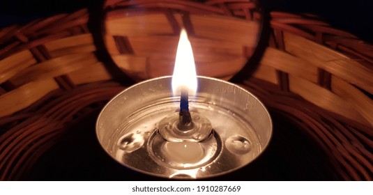 The Flame Of A Burning Tea Candle Against The Silhouette Of A Magnifying Glass In A Wicker Brown Stand, At Night (angle).