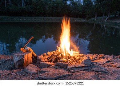 Flame in fire pit with rocks and a hatchet on a stump.