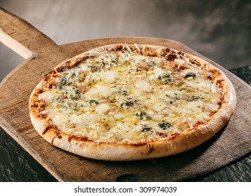 Flame grilled Italian Four Cheeses Pizza served steaming hot on a wooden board in a pizzeria or restaurant for a tasty savory fast food snack or takeaway, close up high angle view