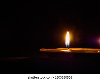 The Flame Of A Lonely Burning Candle In A Puddle Of Wax In The Dark