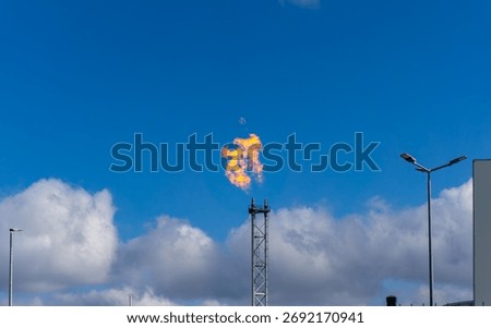 Flame on industrial flare stack against sky and clouds, energy infrastructure, gas emission, industrial installation, environmental impact scene