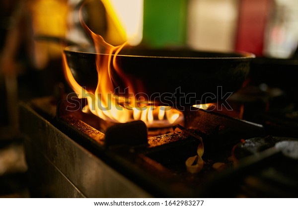 flame\
in the pan. Professional Chef makes flambe for food in the\
restaurant kitchen. Chef cooking with open fire pan.  on a stove.\
Fire burn is cooking on iron pan,stir fire very\
hot