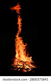 Flame rises vertically at night against deep black background, bright orange bonfire twisting upward with sparks. campfire creates dramatic fire concept, energy and heat symbol, vertical
