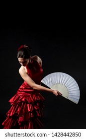 Flamenco Dancer In A Red Lush Dress With A White Fan On A Black Background.