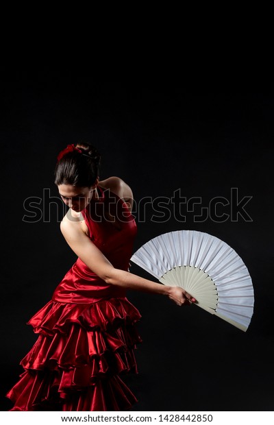 Flamenco dancer in a red lush dress with a\
white fan on a black\
background.