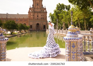 Flamenco Dancer Woman, Beautiful Brunette Teenager Dressed In Typical Costume With Ruffles And Polka Dots Is Dancing By A Canal In A Square In The Park. Flamenco Concept Of World Cultural Heritage.