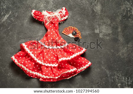 flamenco traditional dress for doll with fan and castanets on a black cement background, top view with copy space