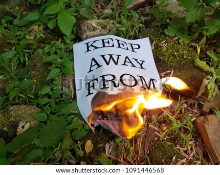 Flames burning a charred piece of firewood and leaping to a burned piece of paper with ruffled ash edges