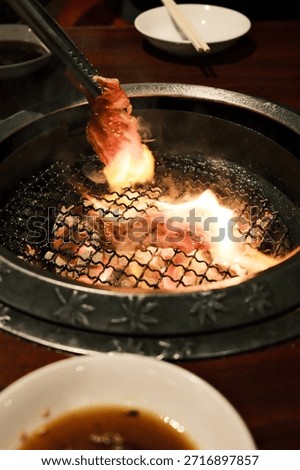 Flames dance beneath marbled beef as chopsticks hover over a tabletop grill, capturing the primal theater of yakiniku.​​​​​​​​​​​​​​​​