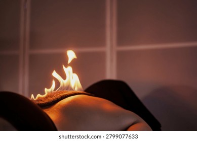 Flames Dancing on a Person's Back During a Fire Massage Therapy. A person lying down on a massage table receiving fire massage treatment. Flames are carefully placed on their back as part of this therapeutic process.